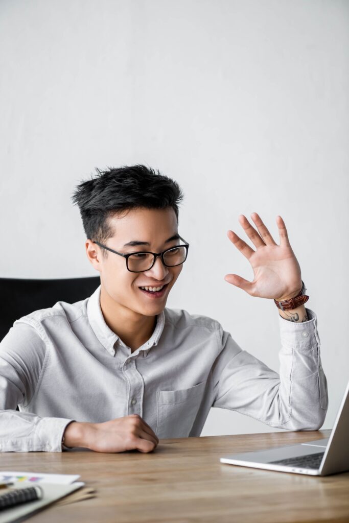 smiling asian seo manager waving during webinar in office